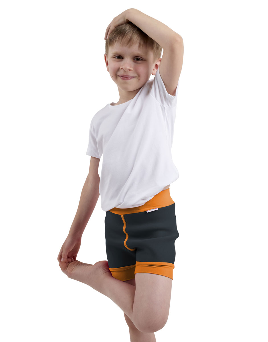 Ein Junge steht mit einem Bein angezogen und einem Arm über dem Kopf. Er trägt ein weißes T-Shirt und eine dunkelgraue Badehose mit orangen Bündchen. Der Hintergrund ist weiß.