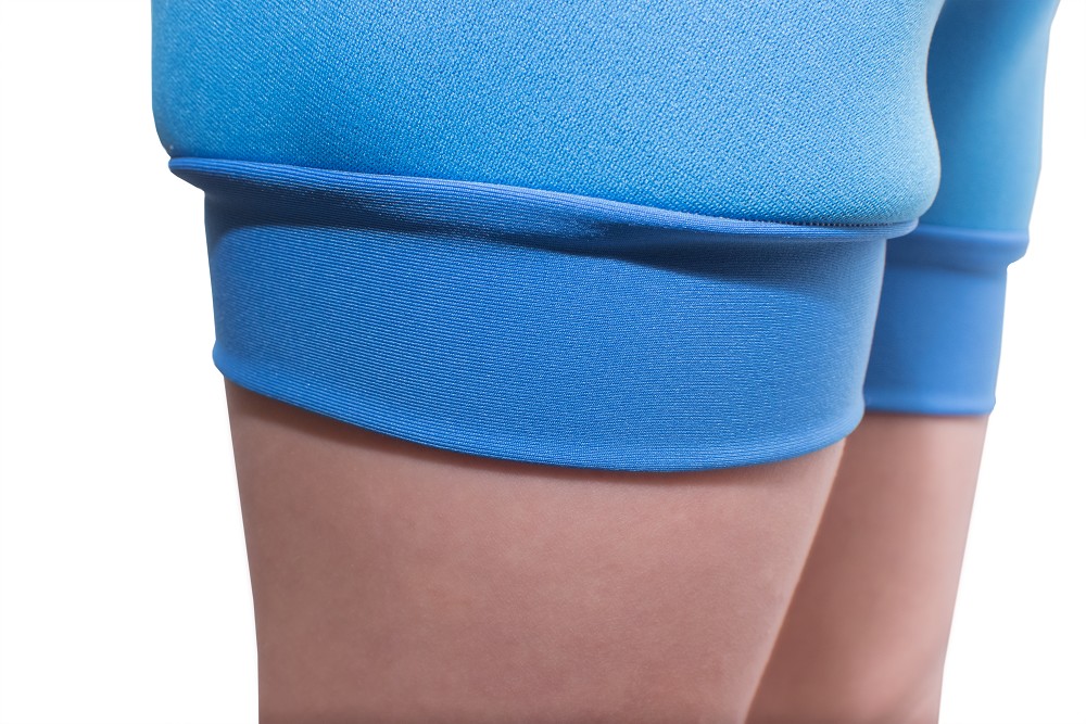 Helle, blaue kurze Sporthose mit elastischem Bund, die eng an den Beinen anliegt. Die Oberfläche zeigt eine strukturelle Textur, während der Hintergrund neutral und unauffällig bleibt.